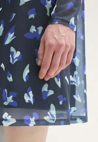 Schwarzes Netzstoffkleid mit einem abstrakten Muster in Blau- und Grüntönen, taillierter Schnitt und einem Saum knapp über dem Knie.