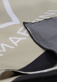 Tessuto beige con testo bianco e bordi neri; texture liscia; piegato con una sezione grigia visibile. Elementi di design moderni evidenti.