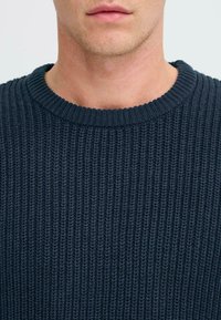 Knitted navy sweater with a crew neckline, featuring a ribbed texture and a fitted design, highlighting the fabric's thickness and warmth.