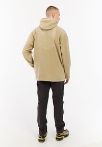 Fleece hoodie in beige met een groot grafisch ontwerp op de achterkant, lange mouwen en een verstelbare capuchon, gecombineerd met donkere broek en schoenen.