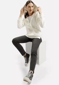 Biała bluza z kapturem na zamek, noszona na szarym topie. Połączona z czarnymi wąskimi dżinsami i czarnymi sneakersami z białymi sznurówkami.