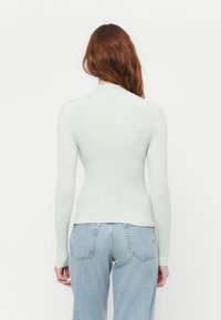 Lys grønn ribbestrikket polokragegenser, tettsittende design, lange ermer og teksturert stoff. Kombinert med lyseblå høytlivsjeans.