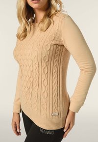 Beige gestrickter Pullover mit einem strukturierten Kabeldesign, langen Ärmeln, geripptem Saum und einem kleinen Markenetikett auf der unteren linken Seite.