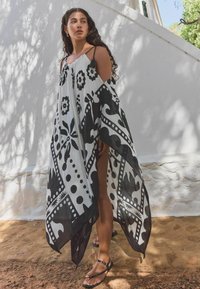 Črno-bela kaftan s pisanjem, izdelan iz lahkotnega materiala, z cvetličnimi vzorci in poudarjenimi detajli. Ima tanke naramnice in svobodnosten silhueto.