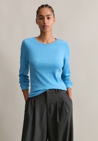 Lichtblauw langemouwen top met een ronde halslijn, gecombineerd met hoge taille grijze geplooide broek met een knoopdetail.