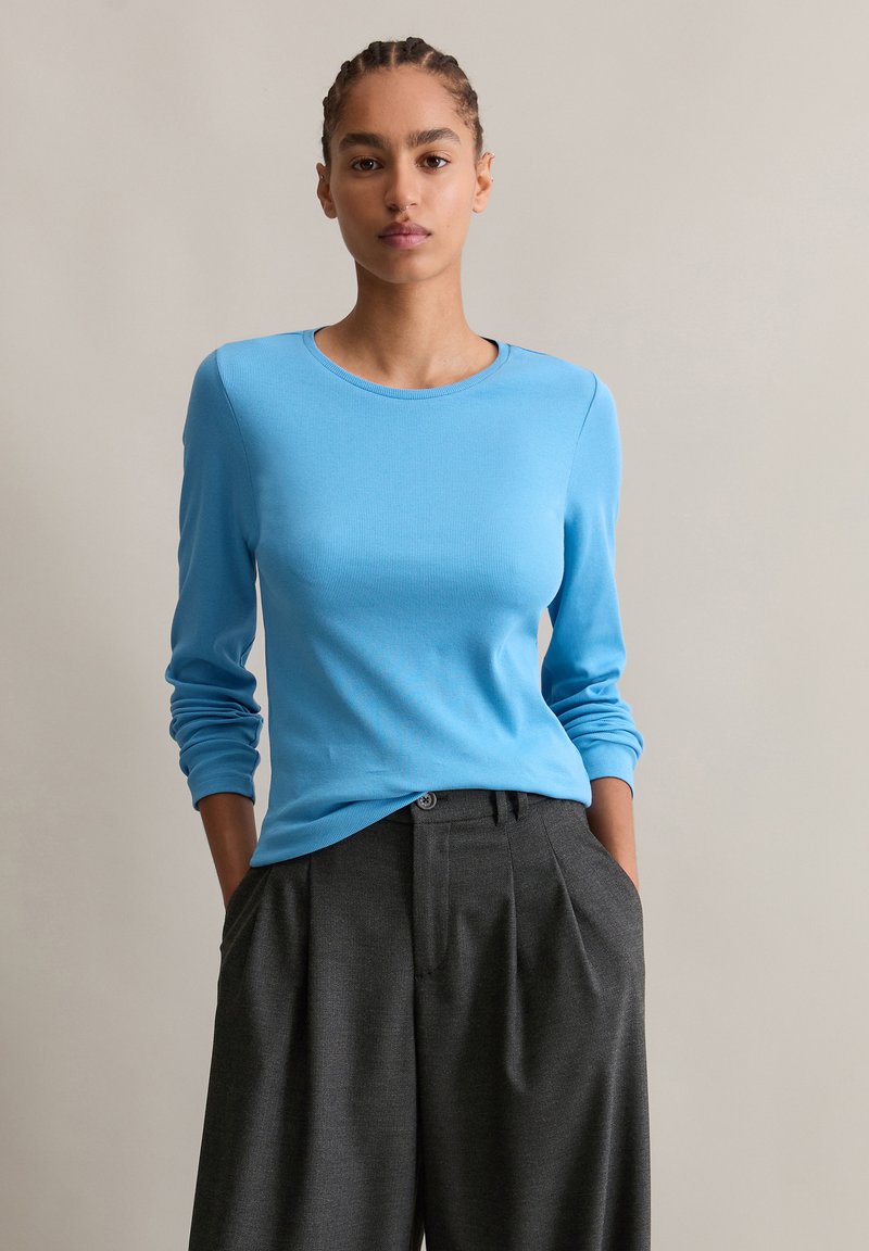 Lichtblauw langemouwen top met een ronde halslijn, gecombineerd met hoge taille grijze geplooide broek met een knoopdetail.