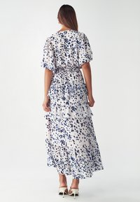 Robe maxi en tissu léger avec un design en couches, présentant des motifs à pois bleu marine et bleu clair sur un fond crème.