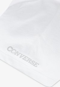 Camiseta de algodón blanca con un logo texturizado en plata de "CONVERSE" cerca del dobladillo, con un acabado suave y limpio.