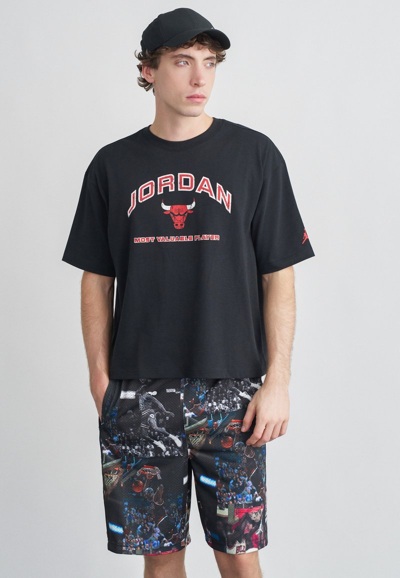 Μαύρο βαμβακερό t-shirt με κόκκινο λογότυπο "JORDAN", σε συνδυασμό με σορτς με σχέδια που απεικονίζουν μπάσκετ σε μαύρους, μπλε και κόκκινους τόνους.
