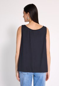 Czarny bezrękawnik z okrągłym dekoltem, uszyty z gładkiego materiału. Luźny krój. Noszony z jasnoniebieskimi dżinsami, widok z tyłu.