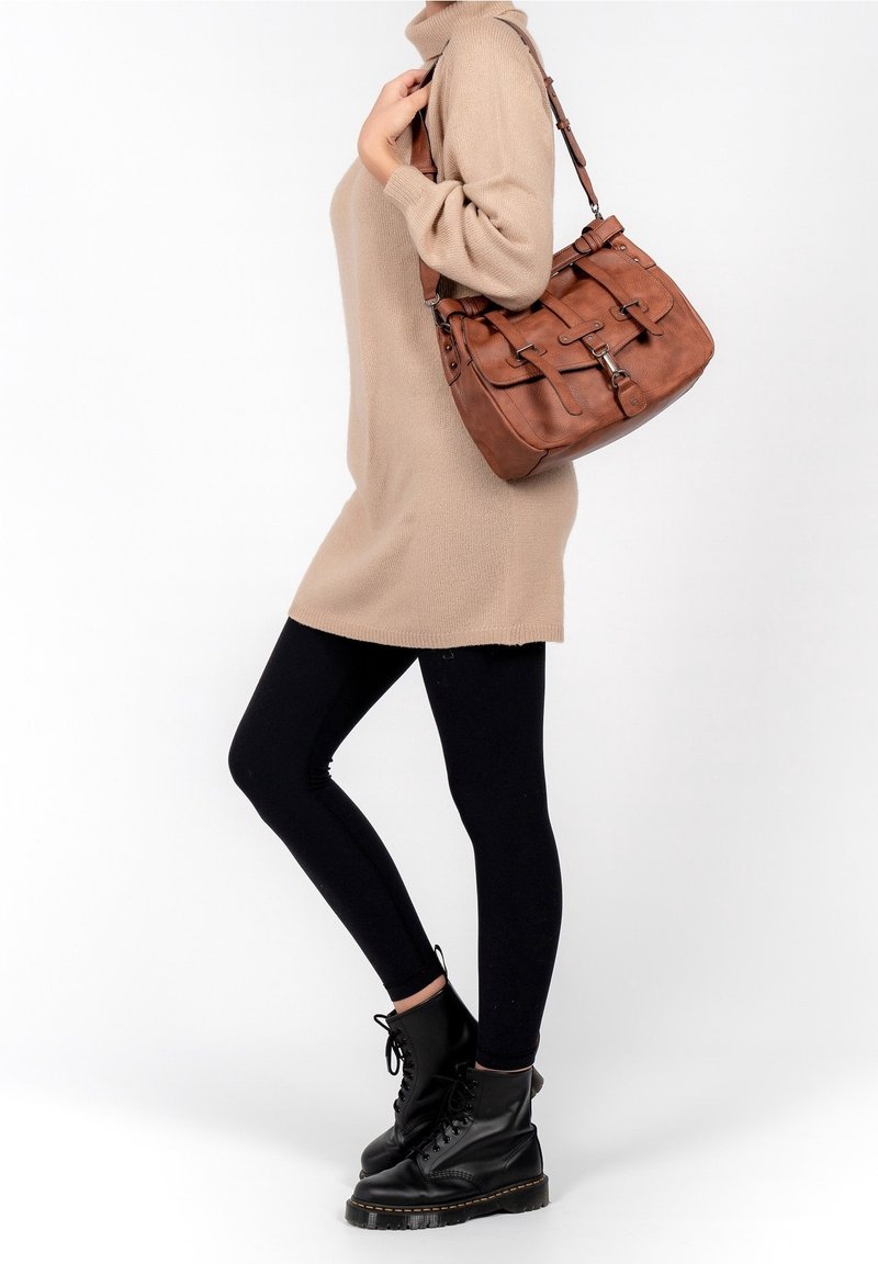 Personne portant une robe-pull beige, des leggings noirs, des bottes noires à lacets, portant un grand sac à bandoulière en cuir marron.