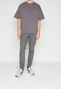 T-shirt gris surdimensionné, à manches courtes ; pantalon gris à motif à carreaux ; baskets blanches et noires avec des accents réfléchissants.