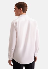 Hvid skjorte med lange ærmer, krave, rund kant og knappede manchetter. Glat tekstur og skræddersyet pasform synlig fra bagsiden.