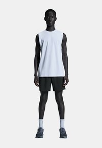 Weißes ärmelloses Sportshirt, schwarze Shorts, graue Sneakers und hellgraue Socken. Glatter Stoff, lockere Passform, minimales Design.