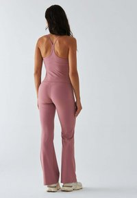 Różowy strój sportowy składający się z dopasowanego topu na ramiączkach typu racerback oraz rozkloszowanych spodni, wykonany z gładkiego, elastycznego materiału.
