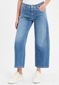 Jean large bleu clair en denim, avec un léger effet délavé, cinq poches et un ourlet droit, accompagnés de baskets blanches.