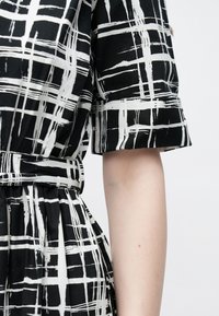 Rochie alb-negru cu model în carouri, cu mâneci scurte și talie strânsă. Țesătură moale, ușoară, cu detalii plisate.