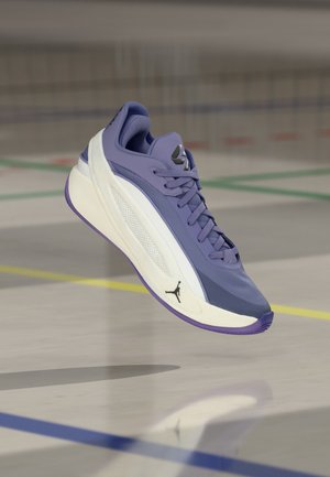 Vijoličen in bel športni copat s črnim logotipom Jumpman, ujet v zraku nad telovadniškim tlemi označenim s pisanim linijami.