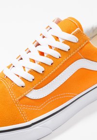 Baskets en toile orange avec des lacets blancs et une bande latérale, dotées d'une semelle en caoutchouc noire et de détails de couture blanche contrastants.