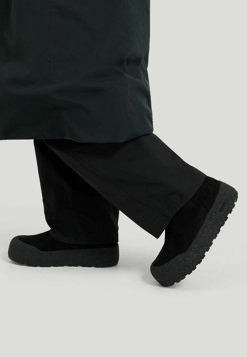 Mustat mokkanahkakengät, joissa on paksut harmaan tekstuuriset pohjat. Yhdistetty löysiin mustiin housuihin, joissa on vähäinen säde nilkan ylle.