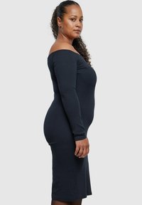 Svart off-shoulder kjole med lange ermer, ribbet tekstur, kroppsnær passform, knelengde og subtile sømdetaljer.