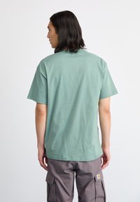 T-shirt de algodão verde com mangas curtas, decote redondo e um corte descontraído, mostrado de costas. O tecido parece macio e suave.