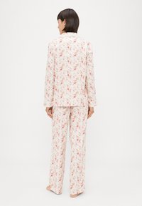 Conjunto de pijama floral com fundo branco e padrões de flores rosa e amarelas. Camisa de mangas longas e calças largas em tecido macio.