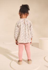 Haut crème à manches longues avec motif floral bleu, leggings rayés roses et chaussures beiges sans lacets. Comprend des poignets volantés et une fermeture boutonnée au dos.