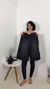 Mustat farkkushortsit, joissa on suora leikkaus, etutaskut ja vetoketjusulku, pidetään henkilöltä neutraalia taustaa vasten.