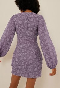 Robe en dentelle florale violette avec de longues manches bouffantes, corsage ajusté et fermeture éclair à l'arrière ; tissu texturé avec un revêtement transparent.