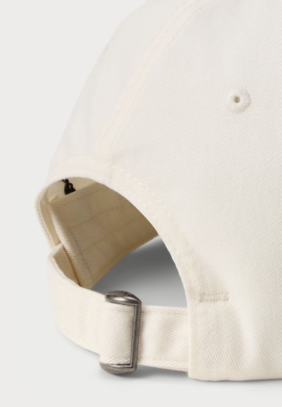 Nastaviteľná béžová baseballová čiapka s textúrovanou tkaninou, prešitými detailmi a kovovým sponou vzadu pre úpravu veľkosti.