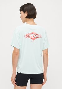 Ljus tealfärgad surftröja med korta ärmar, med en röd "Rip Curl"-logotyp och design på baksidan. Mjuk, slät textur och avslappnad passform.