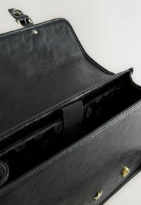 Czarna skórzana torba z fakturowaną powierzchnią. Wnętrze wyłożone wzorzystą podszewką i posiadające dzielący pasek, z mosiężnymi okuciami na klapie.