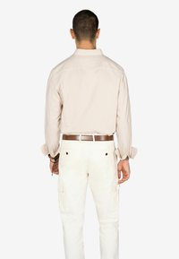 Camisa de cuadros en color beige claro con mangas remangadas, combinada con pantalones cargo blancos. Presenta un cinturón marrón y dos bolsillos traseros.