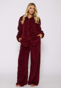 Completo pigiama in pile bordeaux composto da una maglia con bottoni e colletto e pantaloni con motivo. Il materiale è morbido con una finitura testurizzata.