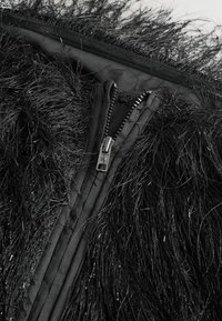 Czarna kurtka z sztucznego futra z długimi, teksturowanymi włóknami, z metalowym zamkiem błyskawicznym i ukrytym zapięciem w kontrastującym gładkim materiale.