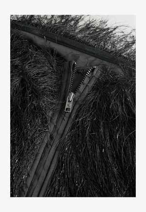 Sort faux fur jakke med lange, teksturerede fibre, med en metal lynlås og skjult lukning i et kontrasterende glat stof.