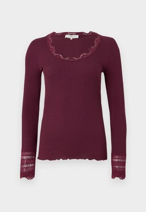 Blusa de manga longa de cor bordô, com decote de renda em forma de escalinhos e detalhes em renda nas mangas. Tecido texturizado com um corte ajustado.