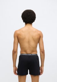 Μαύρο σορτς με λευκό λογότυπο "KARL LAGERFELD" στη μέση. Το ύφασμα φαίνεται �λείο και εφαρμοστό, με απλό σχέδιο χωρίς σχέδια.