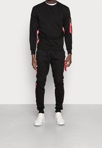 Svart sweatshirt och byxor i set med röda sidodetaljer och vit text. Mjukt tyg, rundad halsringning, ribbade muddar och dragsko i midjan.