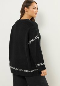 Maglione nero lavorato a maglia con vestibilità ampia. Presenta dettagli in punto croce bianco lungo le maniche e l'orlo. Tessuto testurizzato e polsini a coste.