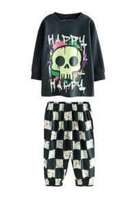 Top nero a maniche lunghe con grafica di teschio verde neon e motivo macchiato colorato, abbinato a pantaloni a scacchi bianchi e neri con schizzi di vernice.