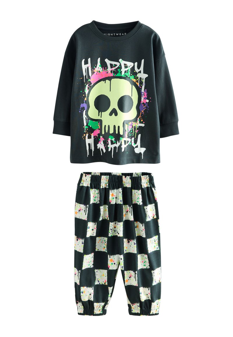 Top nero a maniche lunghe con grafica di teschio verde neon e motivo macchiato colorato, abbinato a pantaloni a scacchi bianchi e neri con schizzi di vernice.