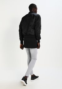 Veste bomber noire avec des poignets côtelés, portée sur un haut noir, un jean gris ajusté et des baskets noires. Texture lisse, design décontracté.