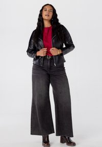 Zwarte leren motorjasje over een rode shirt, gecombineerd met wijde, donkerdenimjeans en bruine haklaarzen. Soepele texturen, minimalistisch ontwerp.