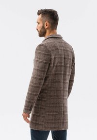 Ruskea ruudullinen takki, jossa on kevyt rakenne, yksirivinen malli, leveät kaulukset ja istuva leikkaus. Tyylikkäitä metallikoristeita hihoissa.