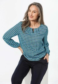 Blusa a maniche lunghe, blu, con un motivo geometrico in verde e nero, caratterizzata da un collo rotondo e un piccolo dettaglio a chiave.