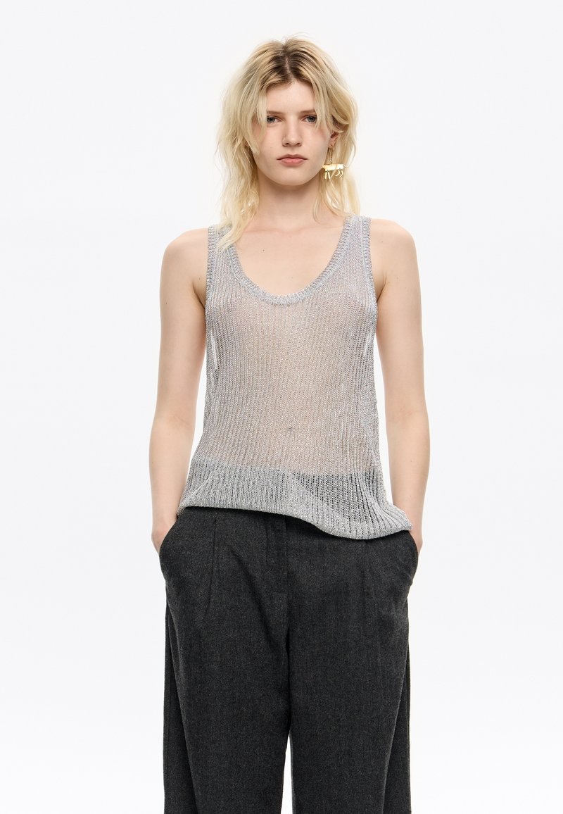 Zilveren mesh tanktop met een ronde halslijn, voorzien van een geribbelde zoom. Gecombineerd met losse, donkergrijze broeken.