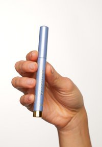 Stylo cylindrique bleu clair avec un accent doré à la base, tenu dans une main. Le matériau semble lisse et métallique avec un minimum de branding.