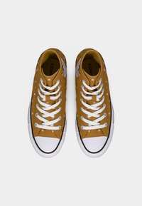 Κίτρινα πάνινα παπούτσια με λευκά αστέρι μοτίβα, λευκά κορδόνια και λαστιχένιες σόλες. Διαθέτουν μαύρες λεπτομέρειες κατά μήκος της σόλας και της γλώσσας.